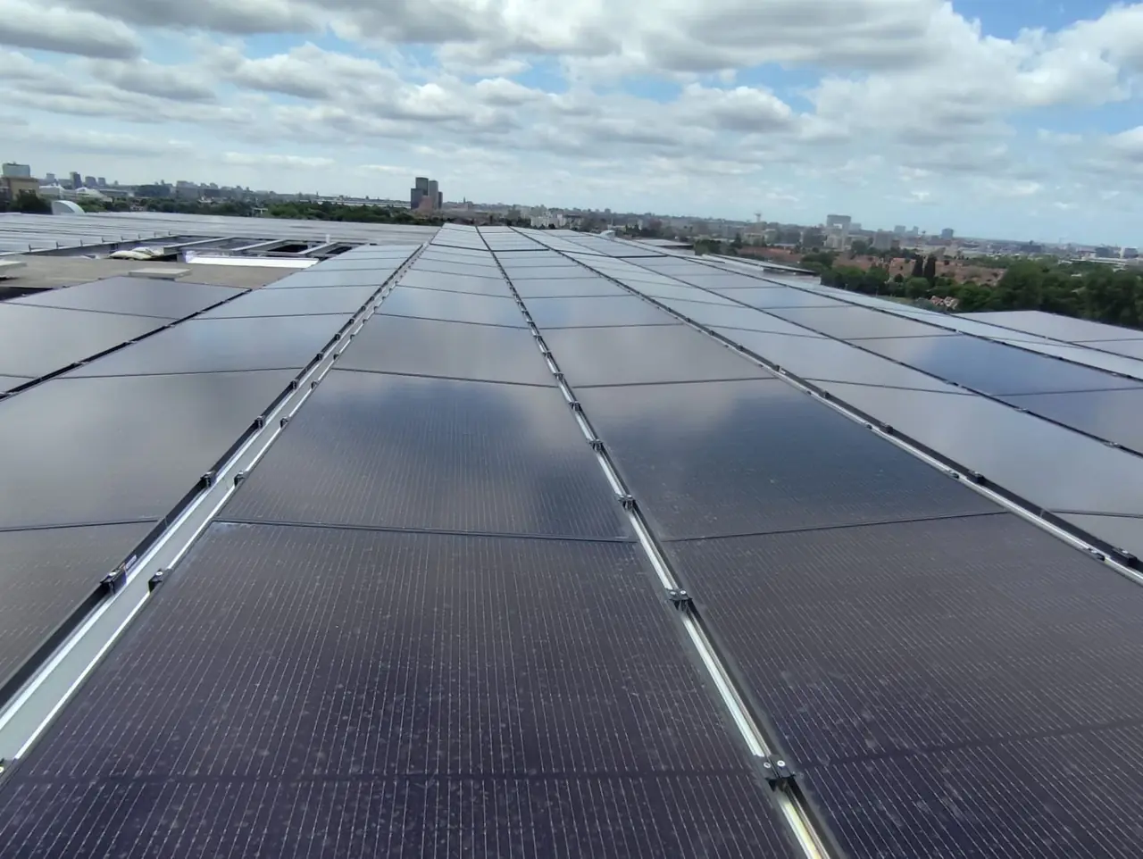 Didelė saulės elektrinė ant pramoninio stogo su miesto panorama